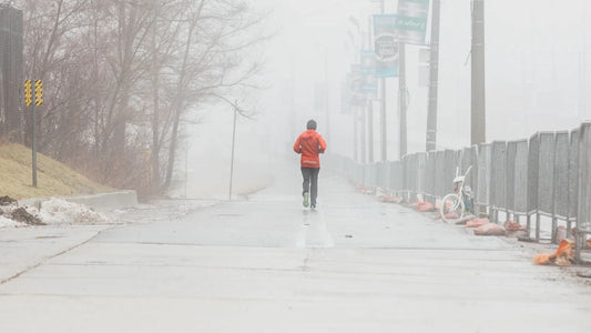 Person in red jacket jogging on foggy road.